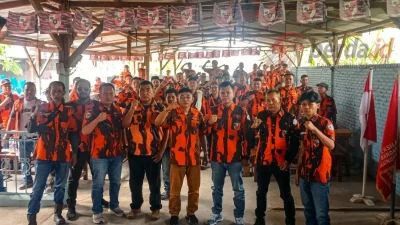 Sekelompok pria berseragam loreng oranye hitam Pemuda Pancasila berdiri bersama di sebuah ruangan dengan bendera merah putih di latar belakang.